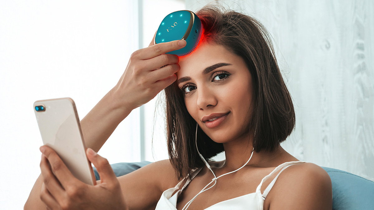 A young brunette using FAQ 301 hair-strengthening scalp massager while listening to music on her phone